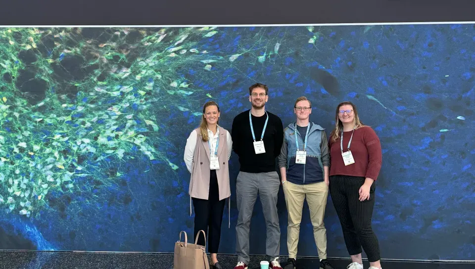 A group of UNE researchers pose in front of a wall with the Society for Neuroscience logo