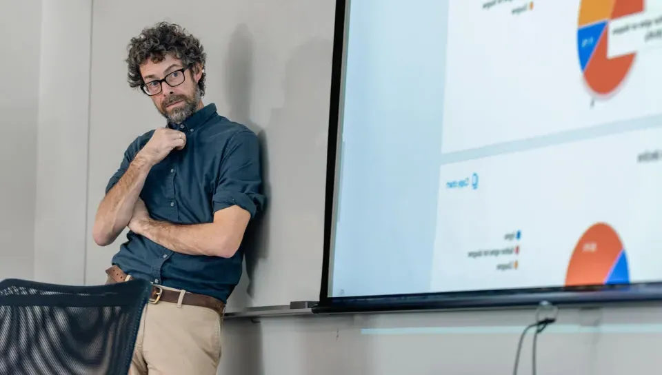 A UNE professor stands against a whiteboard while another professor speaks