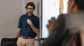 A UNE professor stands against a whiteboard while another professor speaks