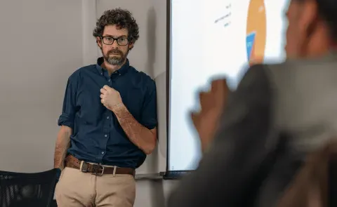 A UNE professor stands against a whiteboard while another professor speaks